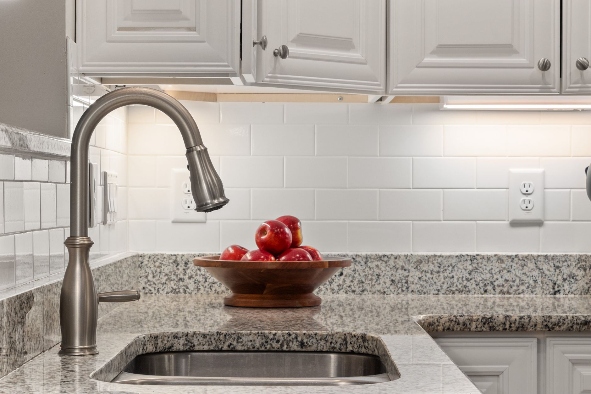 Elegant kitchen countertop featuring fresh apples in a wooden bowl beside a sleek stainless steel sink