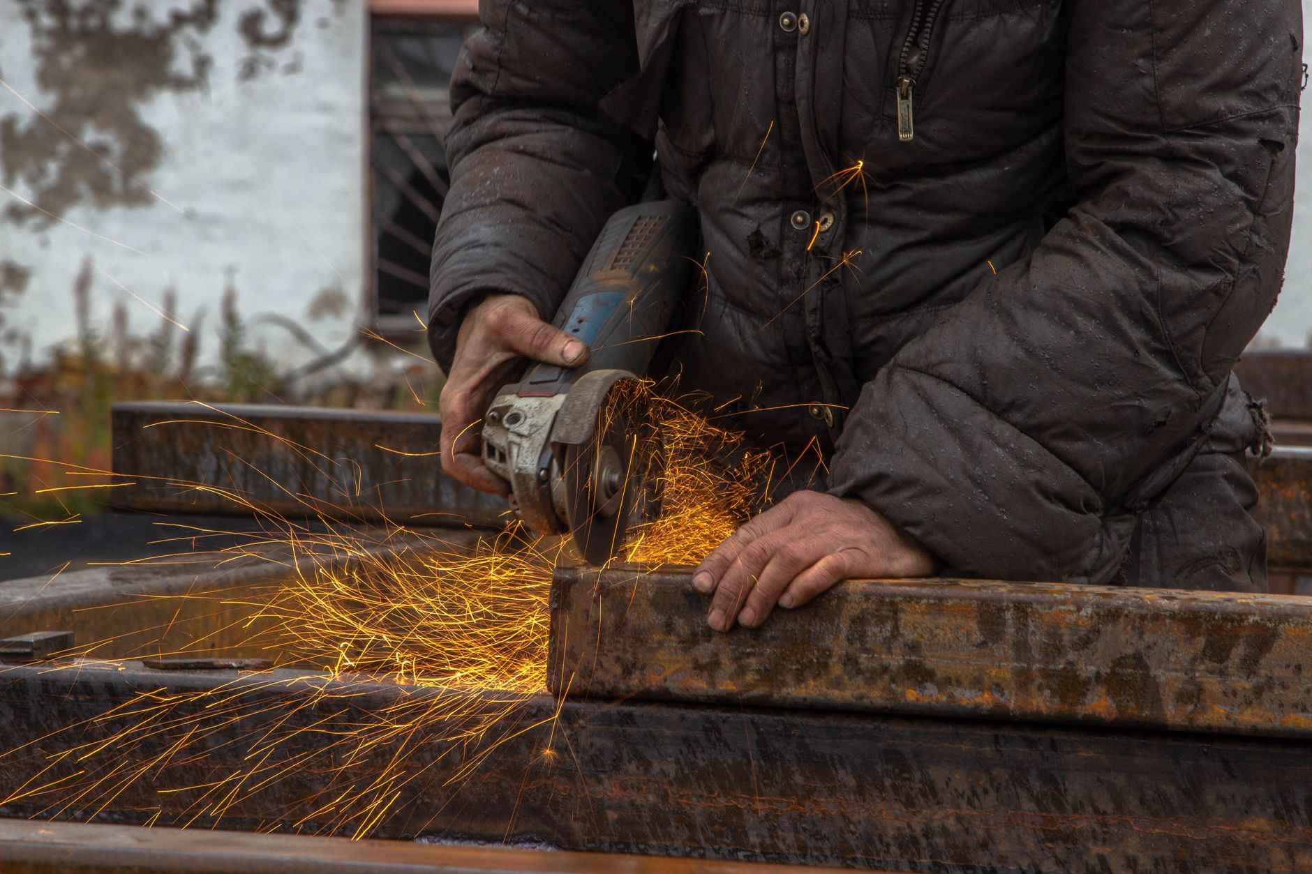Close-up of a worker using a grinder on metal beams, with sparks flying